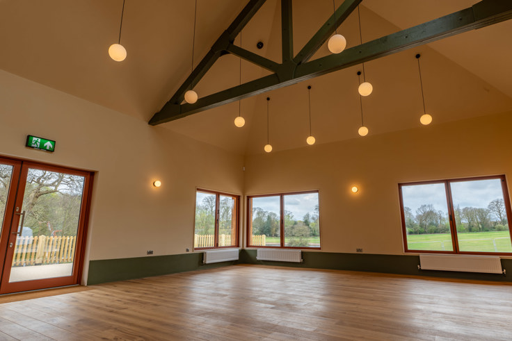 Spacious hall with wooden floor, large windows, exposed beams, and hanging pendant lights.
